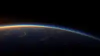 A wide curve of Earth shows a glowing gold-blue atmospheric rim above ocean and cloud, cinematic Blue Planet wallpaper