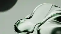 Soft kidney-shaped blob of emerald glass resting on pale studio ground with a faint round shadow upper left, Liquid Emerald wallpaper