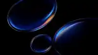 Four tilted blue glass ellipses drifting on pitch black, prismatic rim flares catching amber and violet, Prismatic Orbs wallpaper
